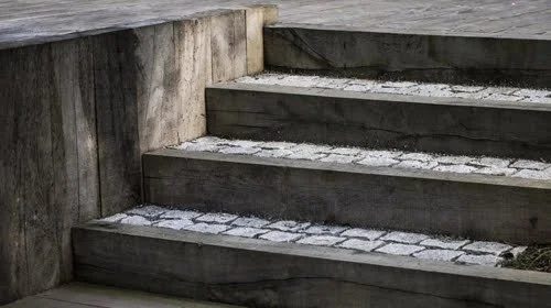 Snow-covered outdoor wooden stairs with concrete walls.