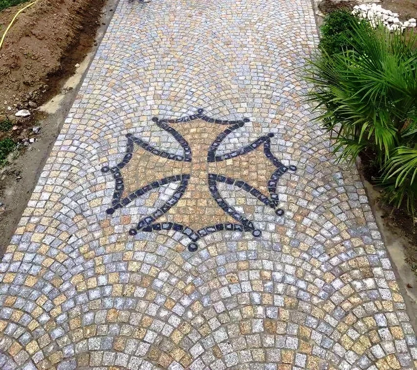 Decorative cobblestone pathway with an intricate mosaic pattern and green plants on the right side.