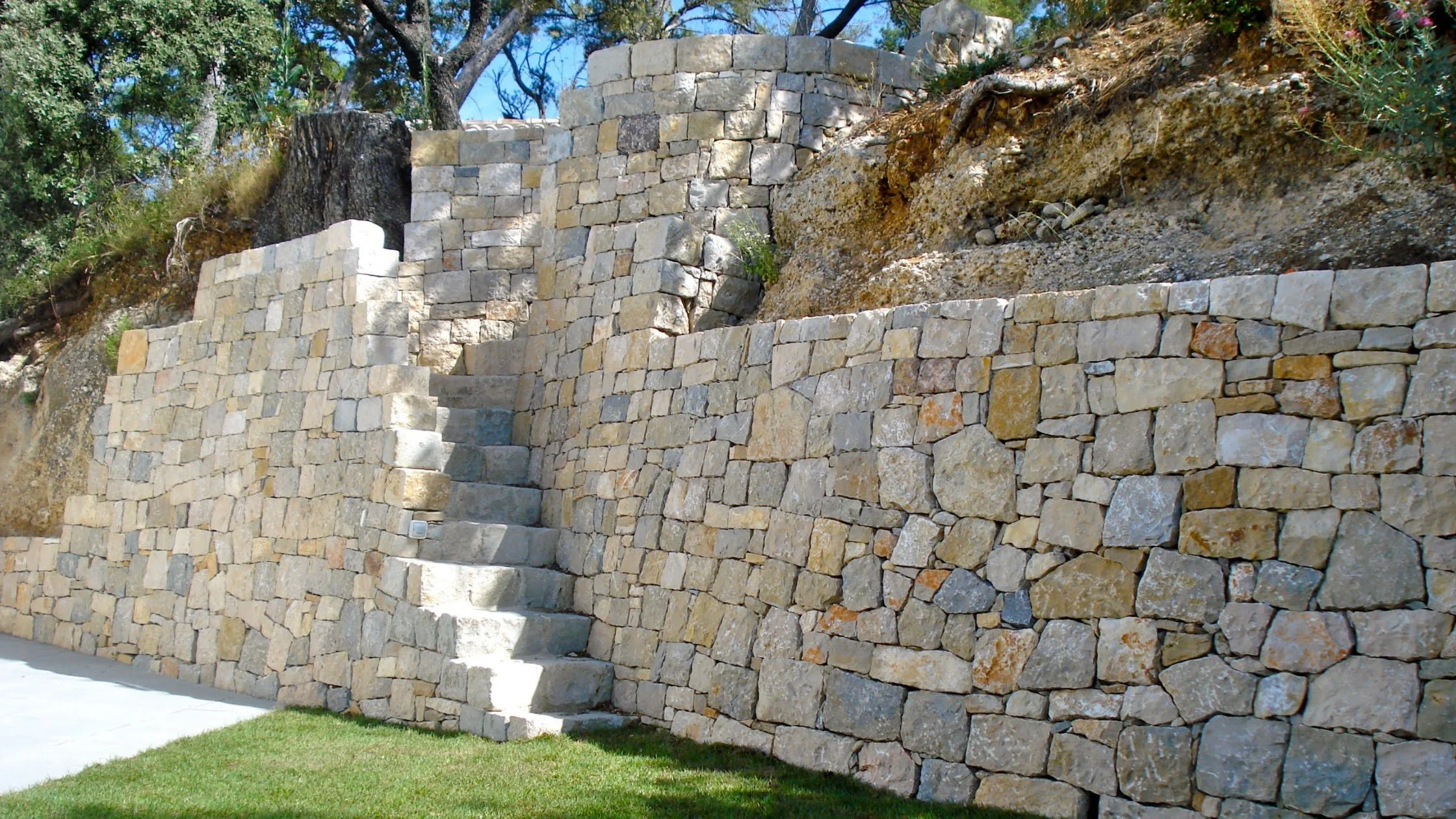 Stone retaining wall with stairs and lush greenery in the background.