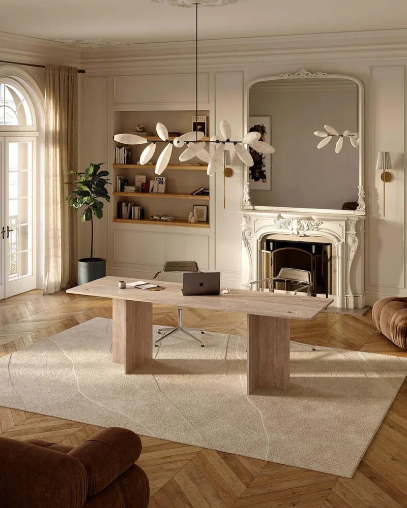 Office room with wooden floors, a large rug, a limestone desk, and a fireplace with marble surround. Large windows with sheer curtains let in natural light.