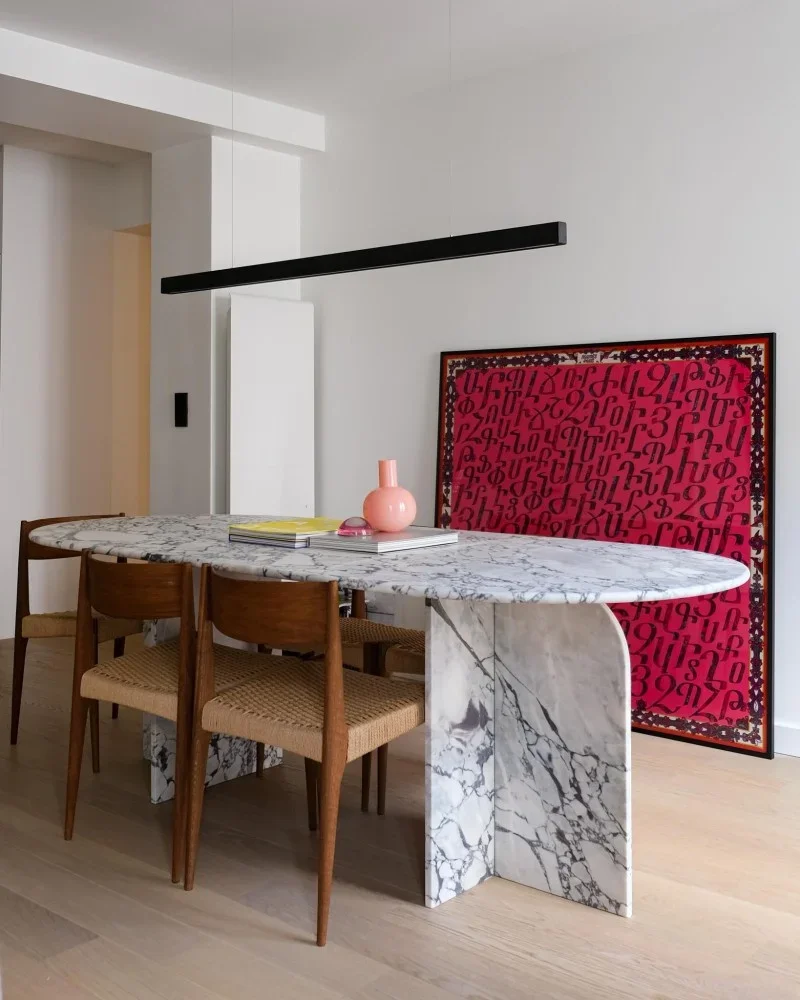Dining room with wooden floors & chairs, a white marble table, a black light fixture and red painting on white walls