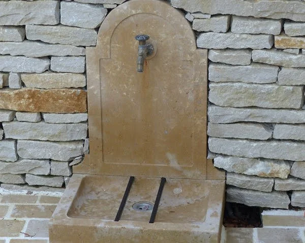 Stone outdoor fountain with a tap and a basin, set against a stone wall.