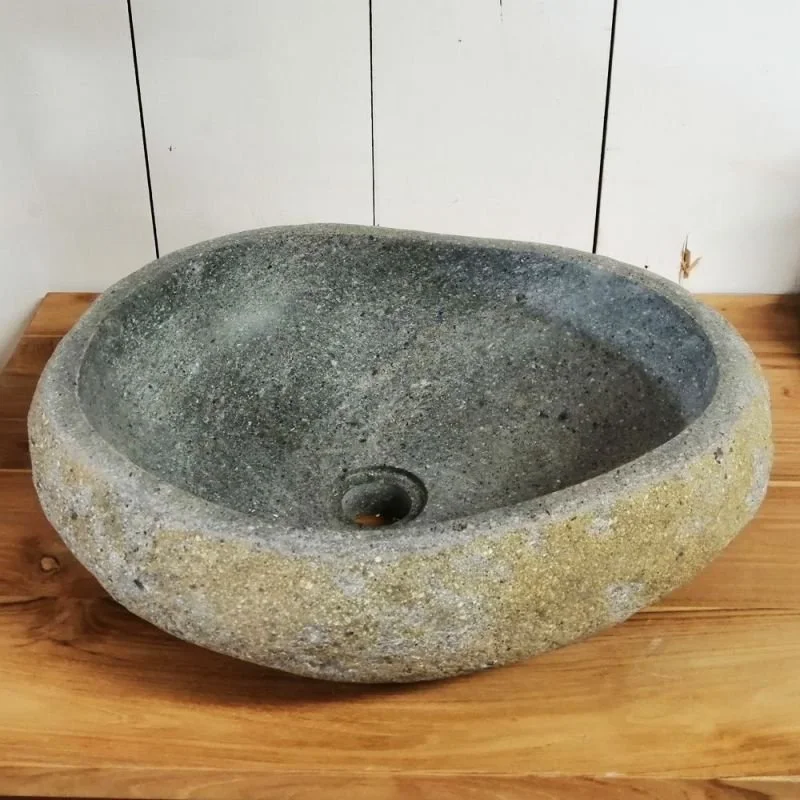 A round stone basin with a rough, textured surface, sitting on a wooden table against a white paneled wall.