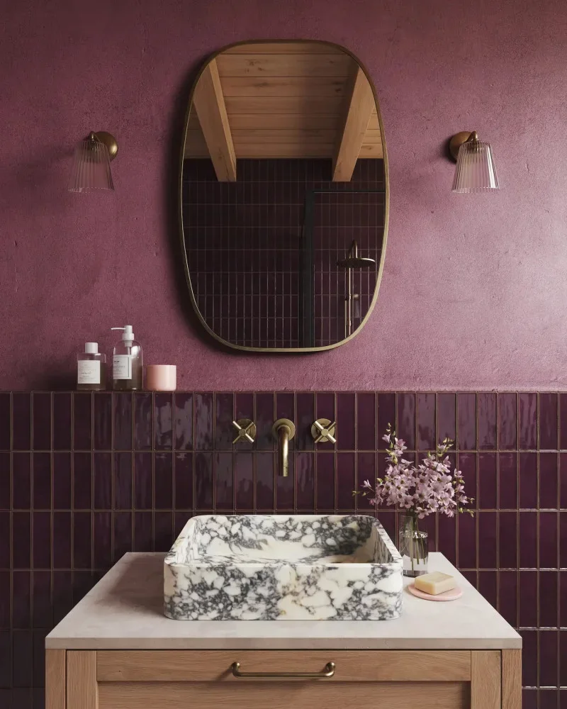 A burgundy bathroom with a marble sink on top a wooden vanity 