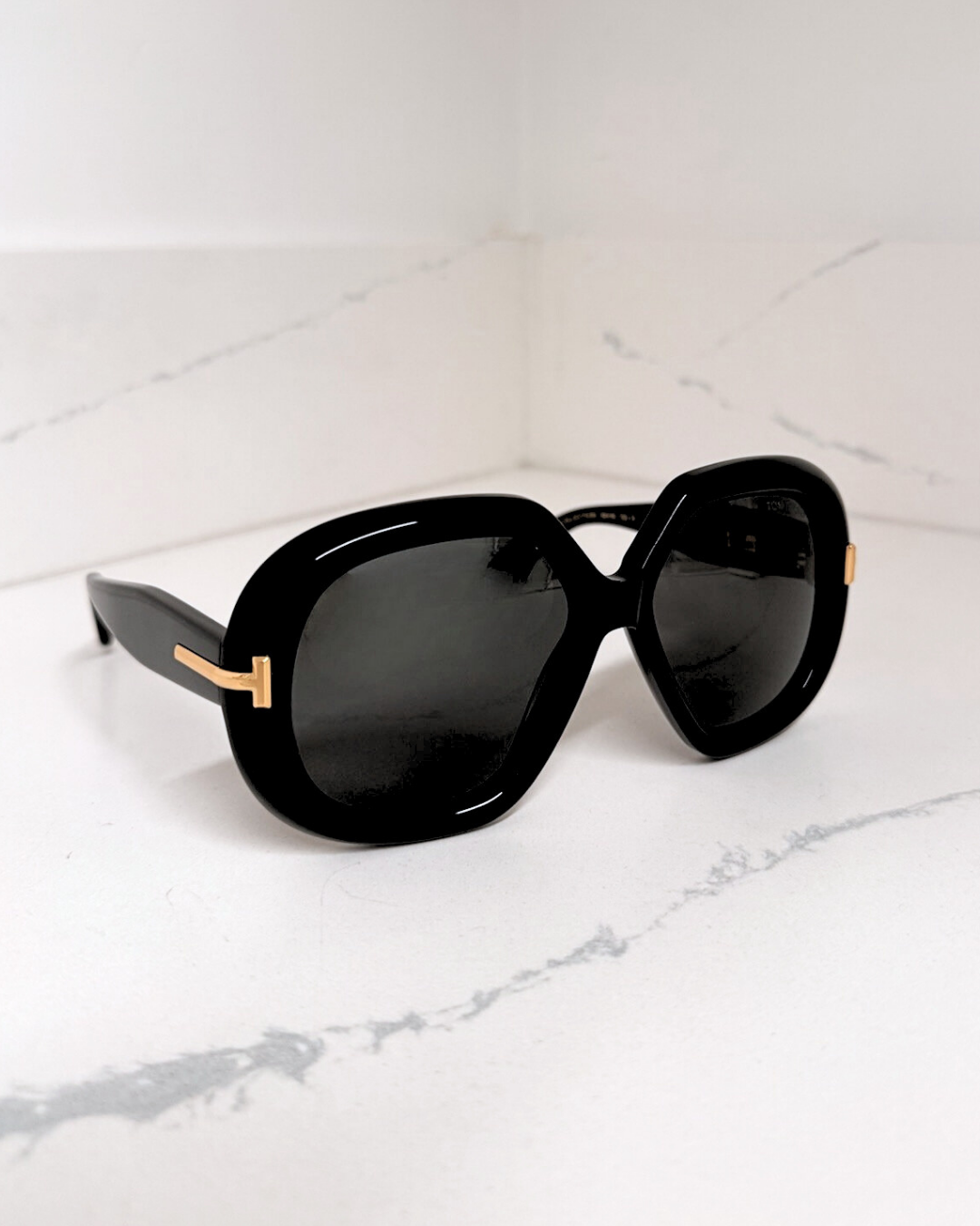 Black sunglasses with large frames and dark lenses on a white marble surface.