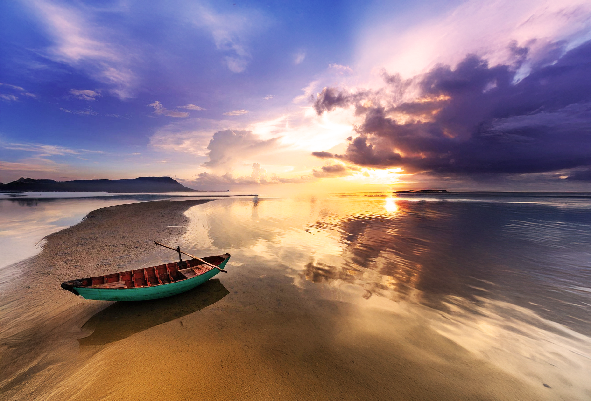 A boat resting on a sandy beach during sunset, with clouds and reflections on the water.