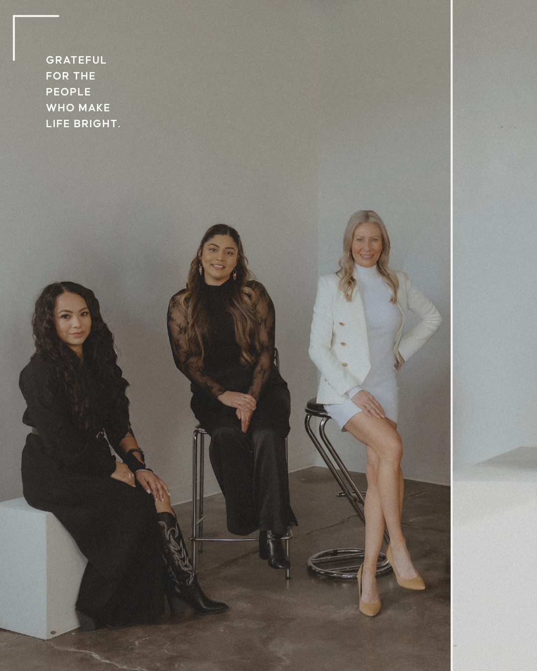 Three women sitting on stools against a plain wall, dressed in black and white, with a motivational quote in the upper left corner that reads, "Grateful for the people who make life bright."