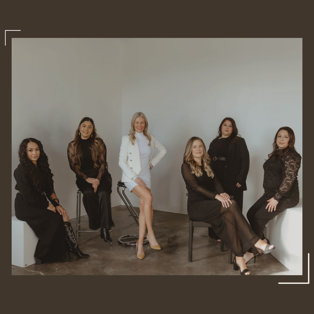 Six women in black and white outfits posing in a minimalistic studio with white and brown walls.
