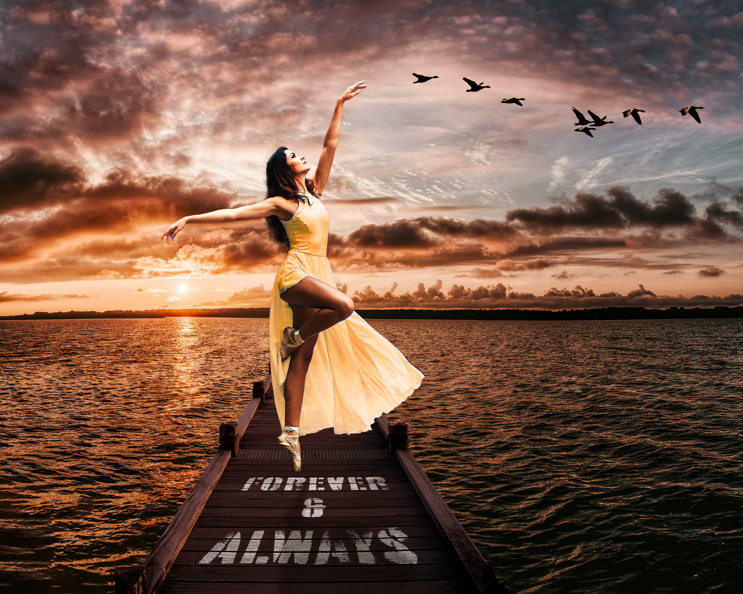 A woman in a yellow dress is dancing on a wooden dock labeled "FOREVER & ALWAYS" at sunset, with clouds and birds flying in the sky over a body of water.
