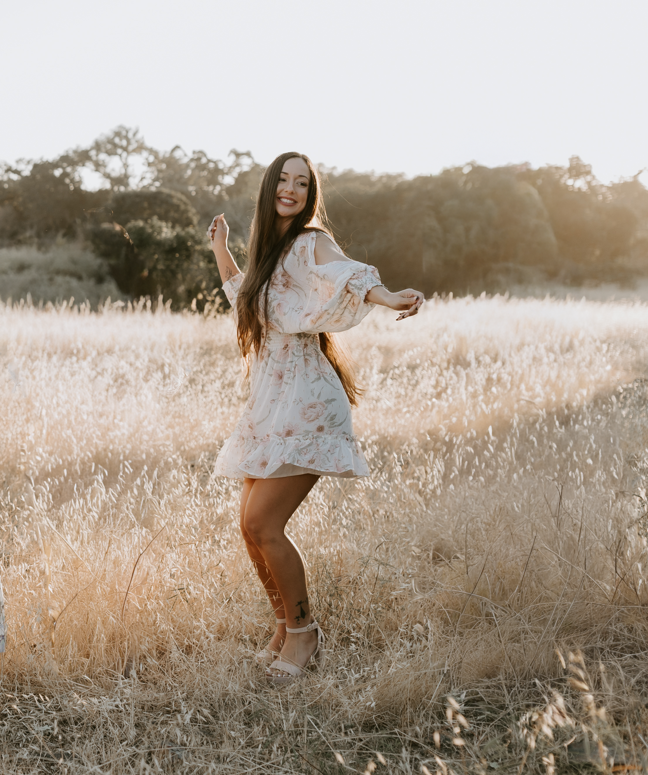 Portrait of Andrea Thompson in a sunlit field, wearing a light floral dress, representing a calm and creative visual aesthetic.