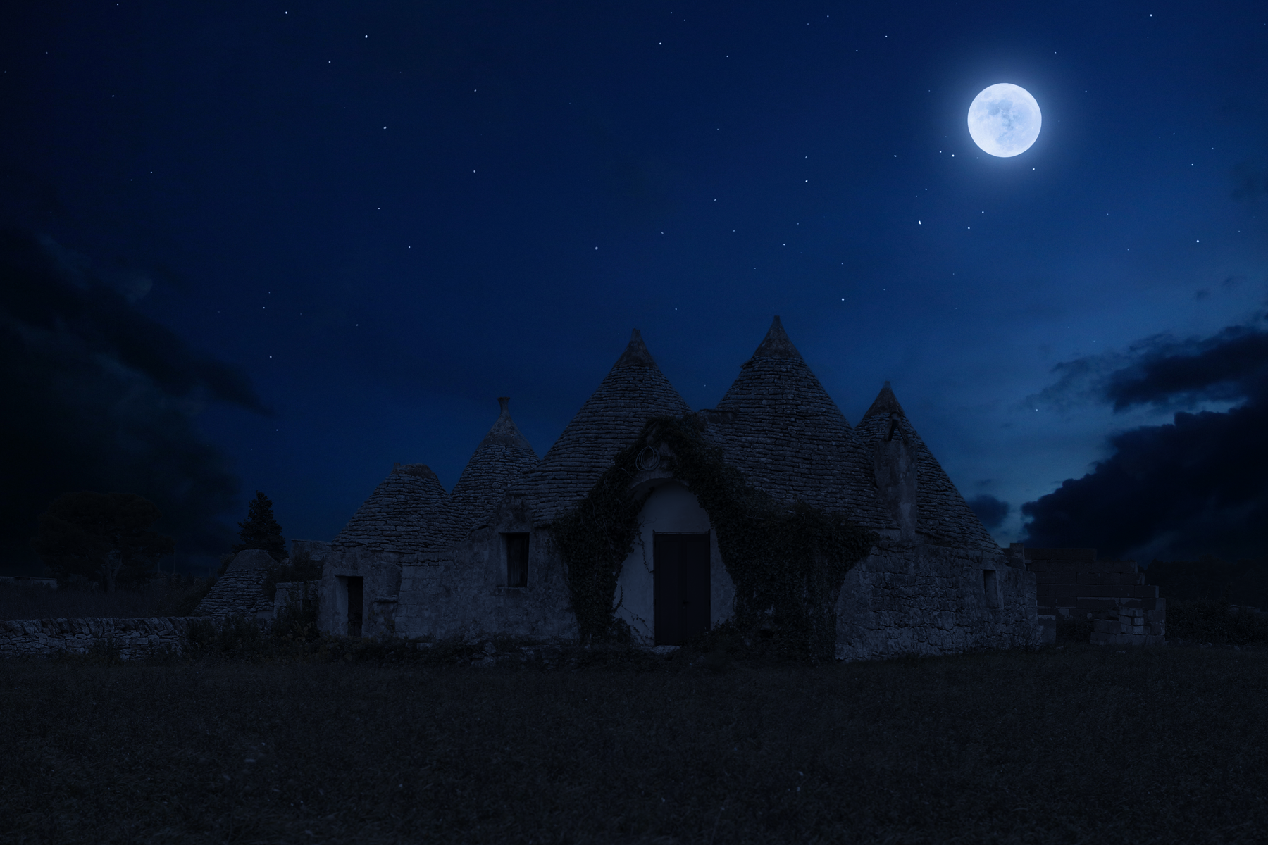 A stone house with conical roofs under a night sky with a full moon and stars, surrounded by dark clouds.