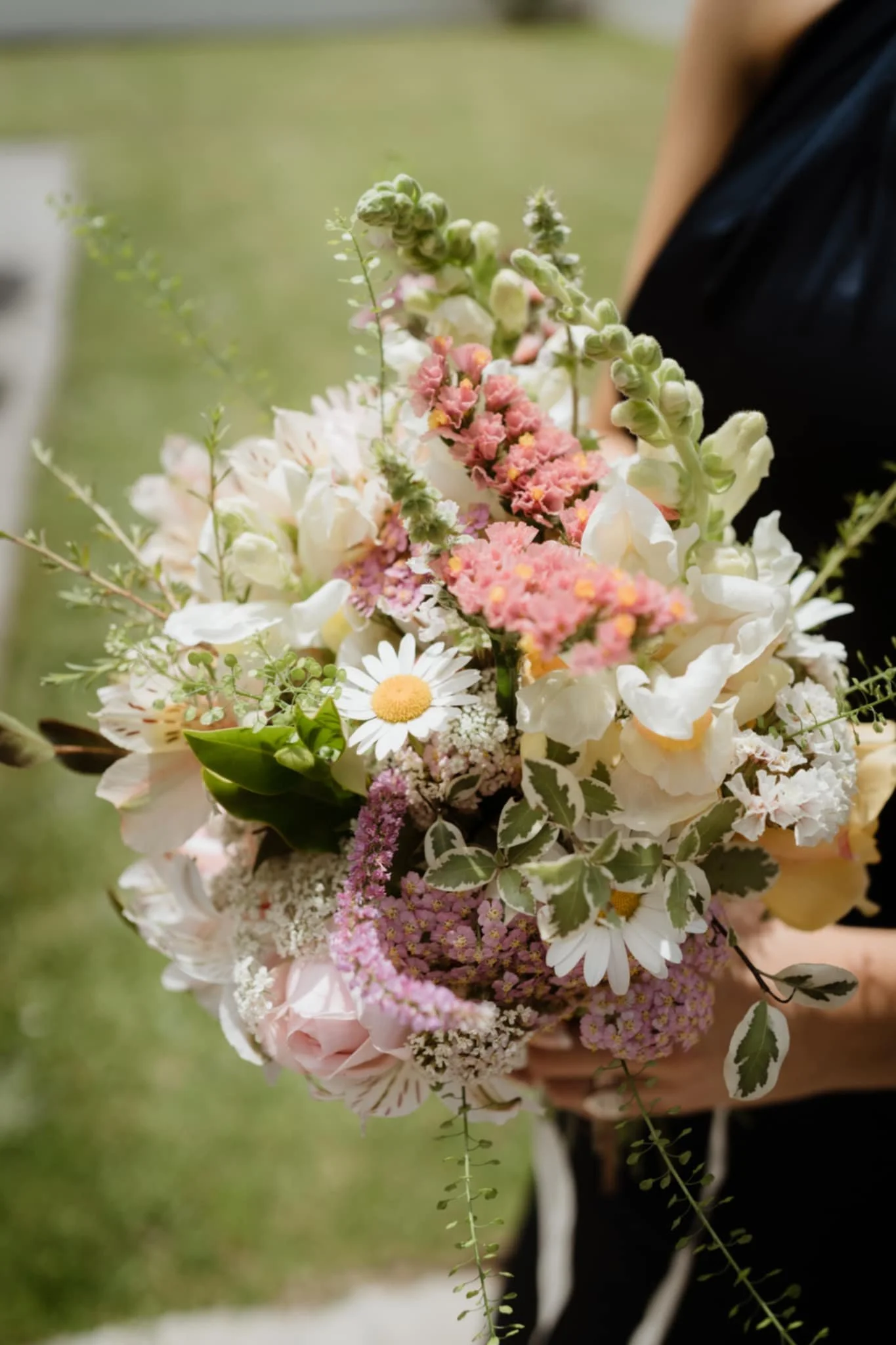 Bridesmaid holding a bouquet of mixed flowers including daisies, roses, and other blooms at an outdoor wedding in Pirongia, near Te Awamutu.