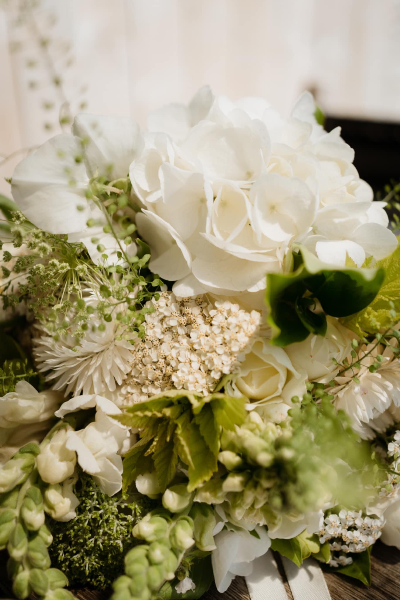 A wedding bouquet of white flowers including hydrangeas, roses, and other blossoms with greenery, resting on a wooden surface in Te Awamutu