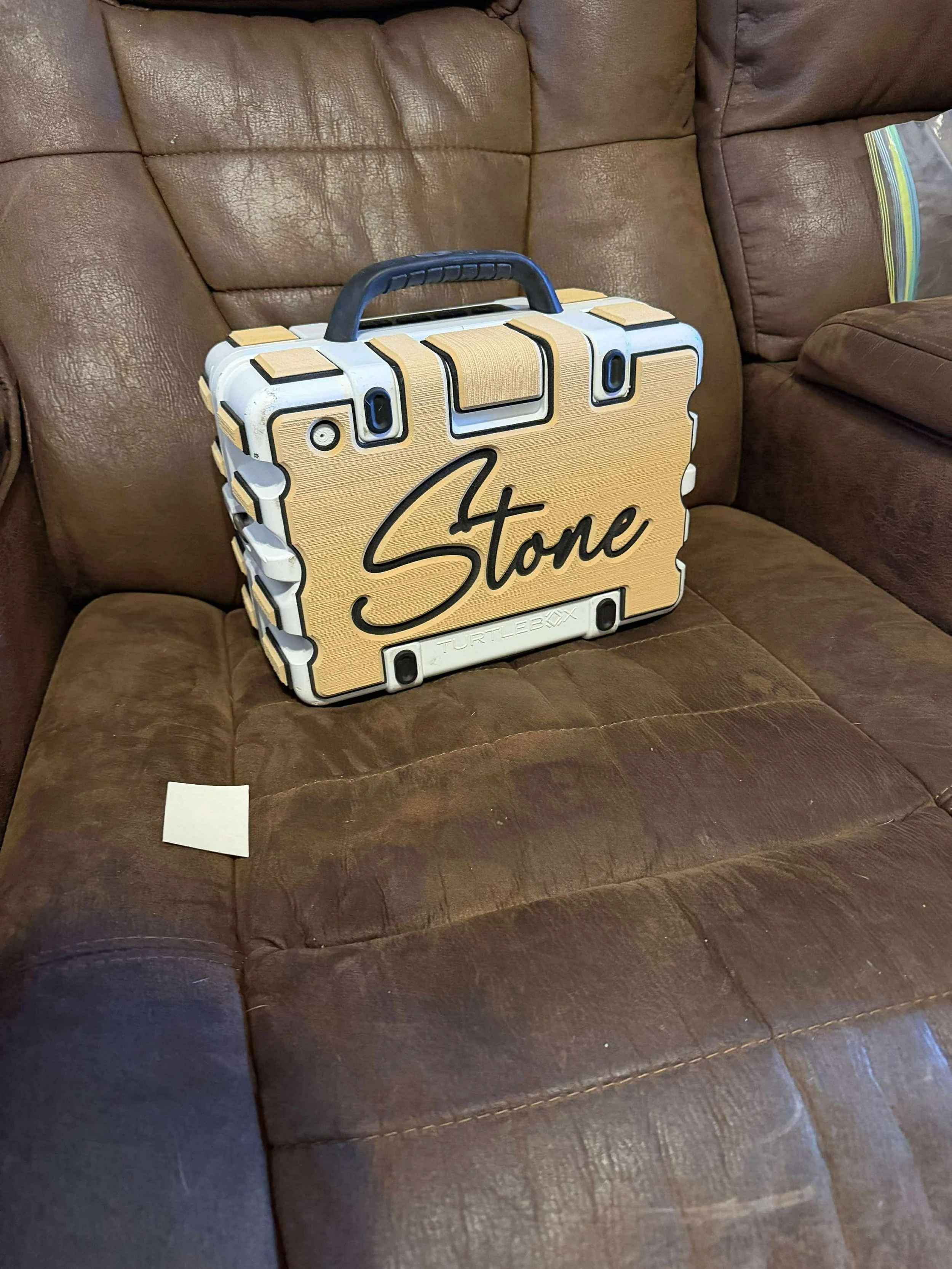 A tan and white box labeled 'Stone' resting on a brown leather couch.