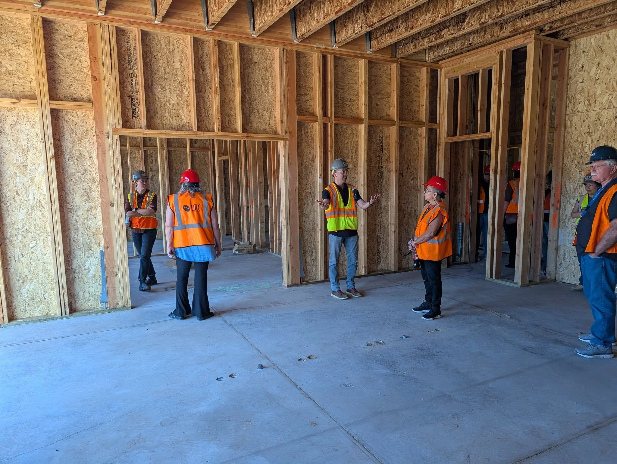 Image of building under construction, people with orange vests and hard hats.