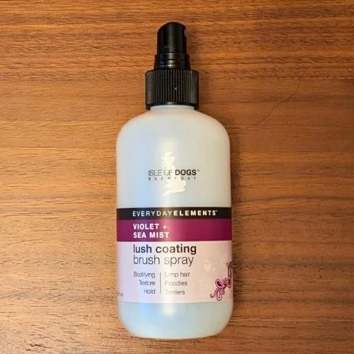 Bottle of Isle of Dogs Violet Sea Mist lush coating brush spray on a wooden surface.