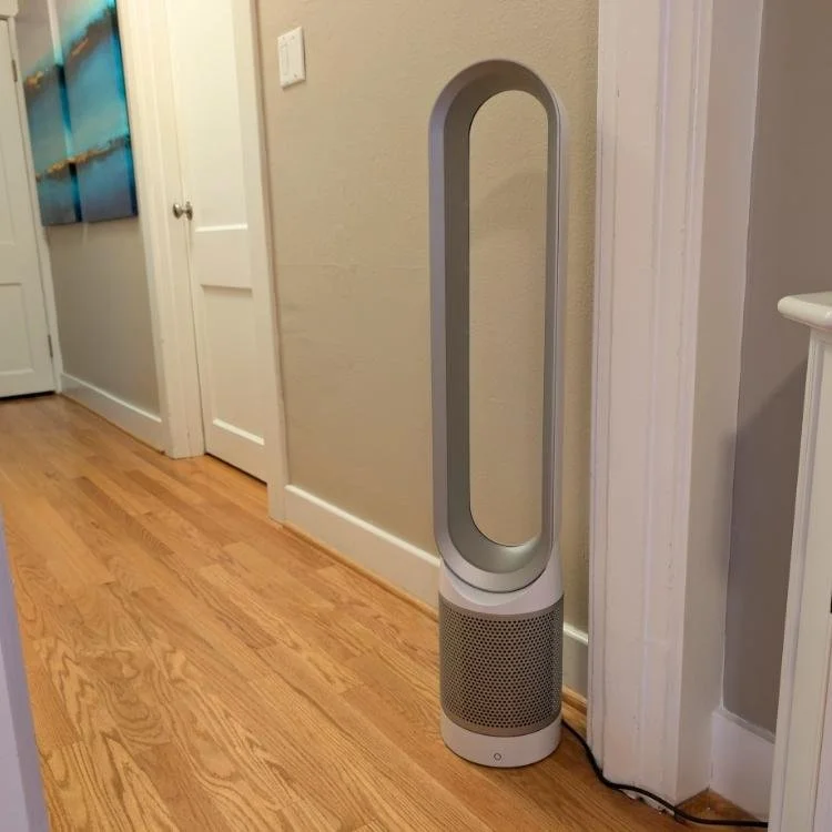 A bladeless tower fan in a room with hardwood floor and beige walls.