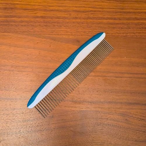 A metal greyhound comb with a blue and white grip on a wooden surface.