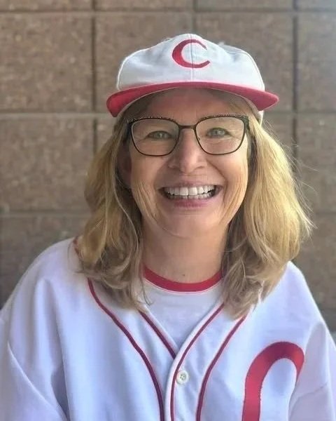 Jean LS. Patrick is dressed as Jackie Mitchell smiling in a Chattanooga Lookouts replica baseball uniform and cap with a red 'C' logo, glasses, and blonde hair.