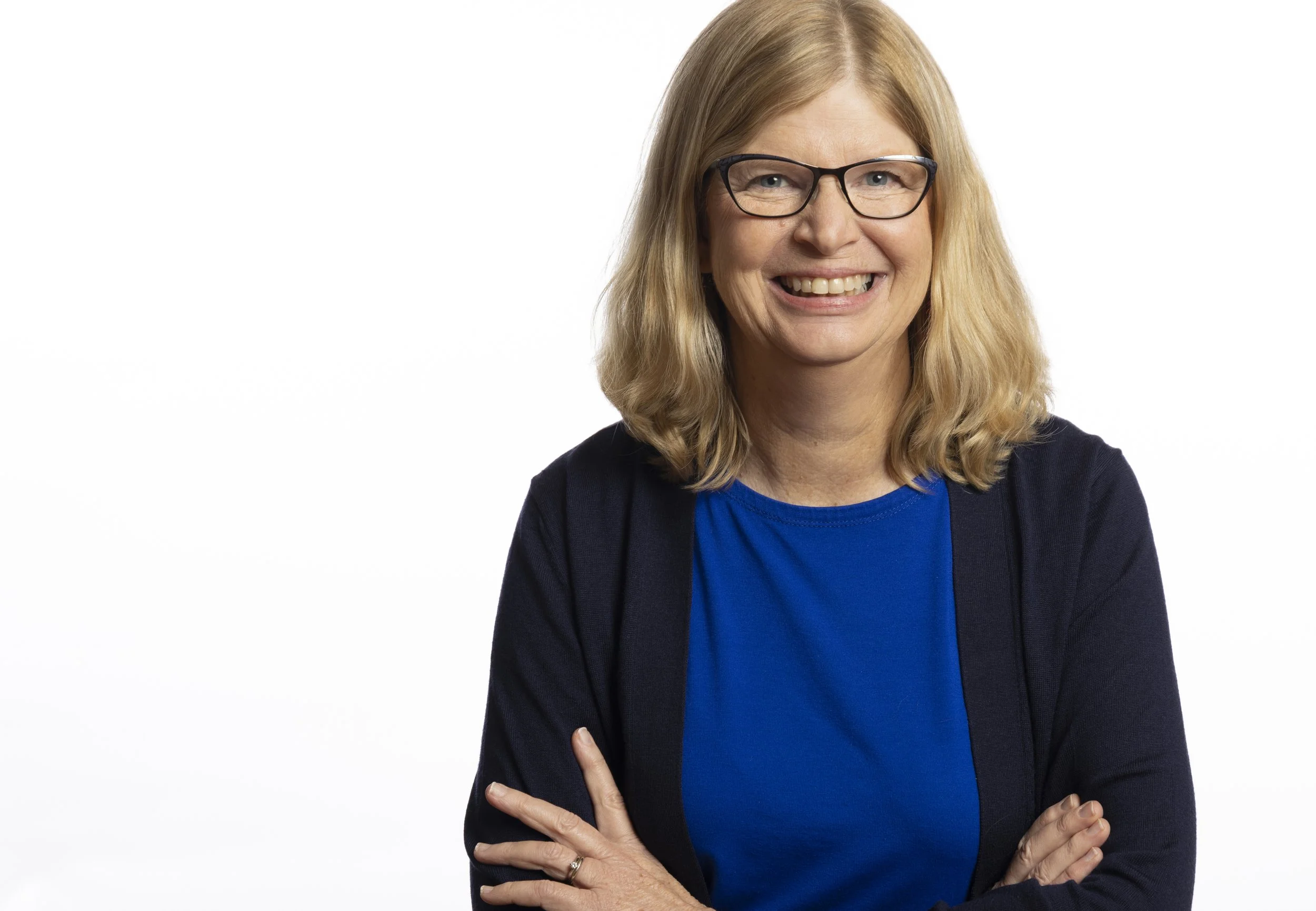 Author Jean L.S. Patrick is a middle-aged woman with blonde hair, wearing glasses, a blue shirt, and a dark jacket, smiling with arms crossed in front of a plain white background.