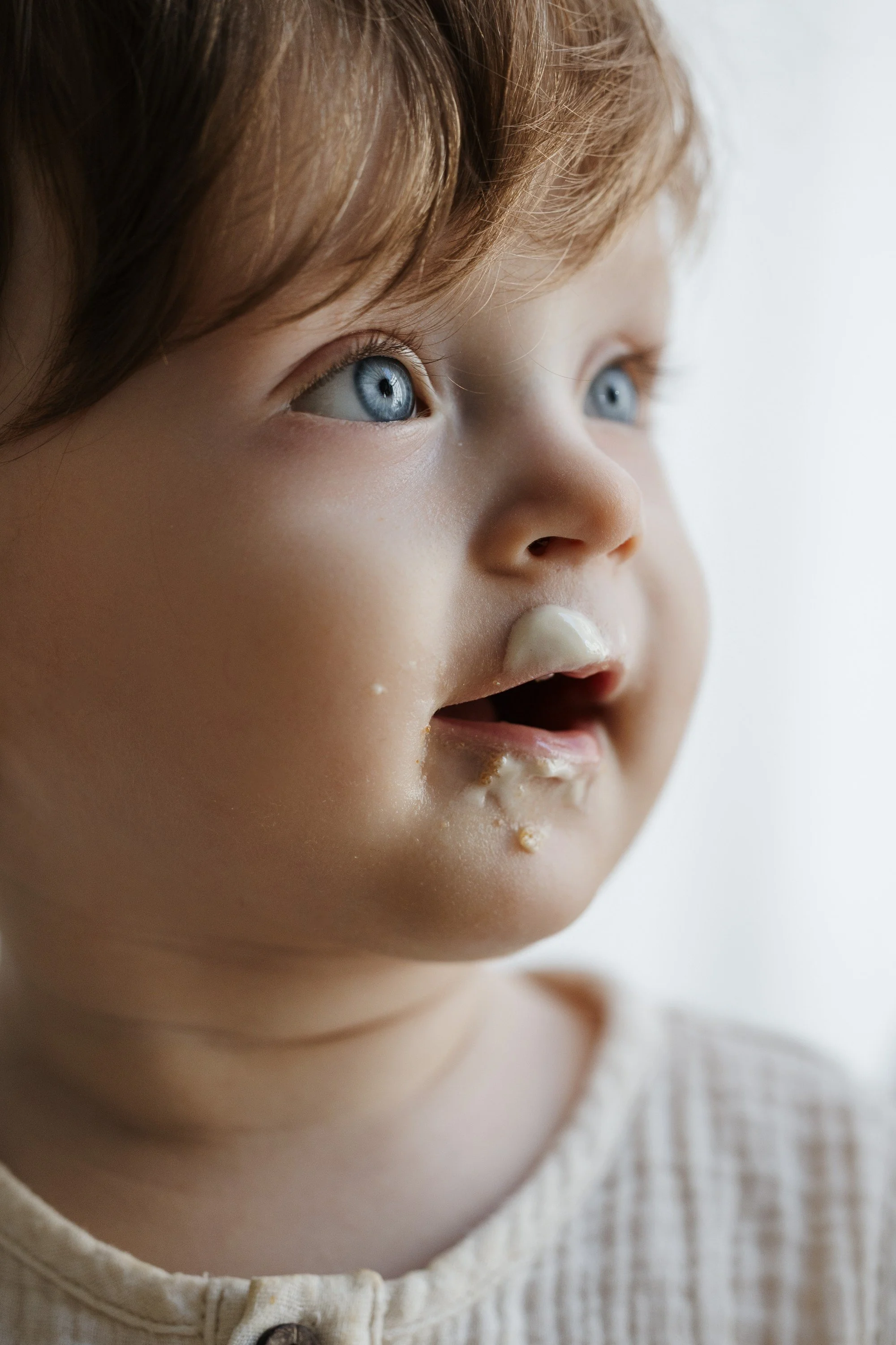 Close-up of a young child's face with blue eyes, messy face, and some food crumbs around the mouth.