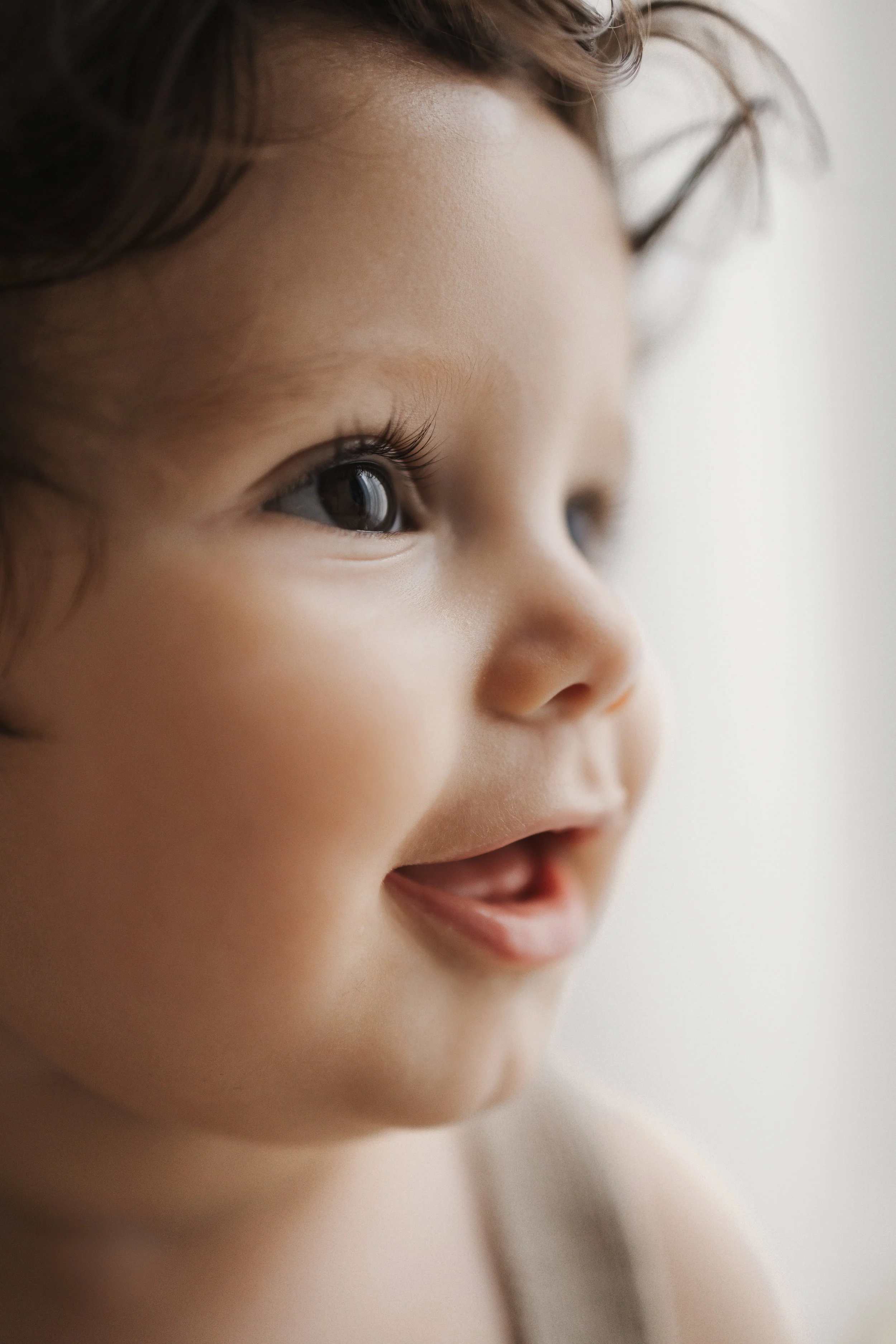 Close-up of a smiling young child with light skin and dark, curly hair looking to the right.