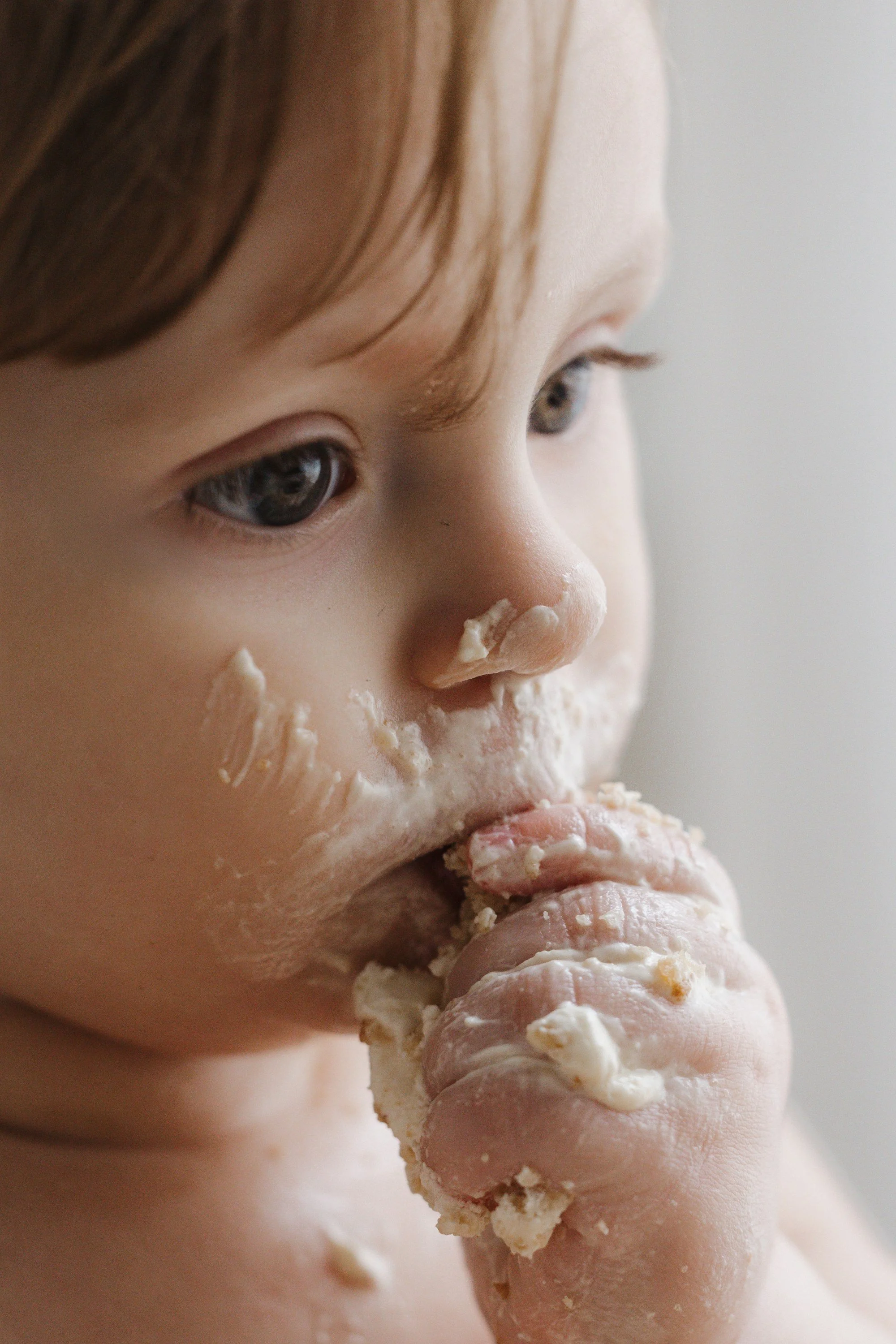 Close-up of a young child with food around her mouth, eating a piece of bread or biscuit.