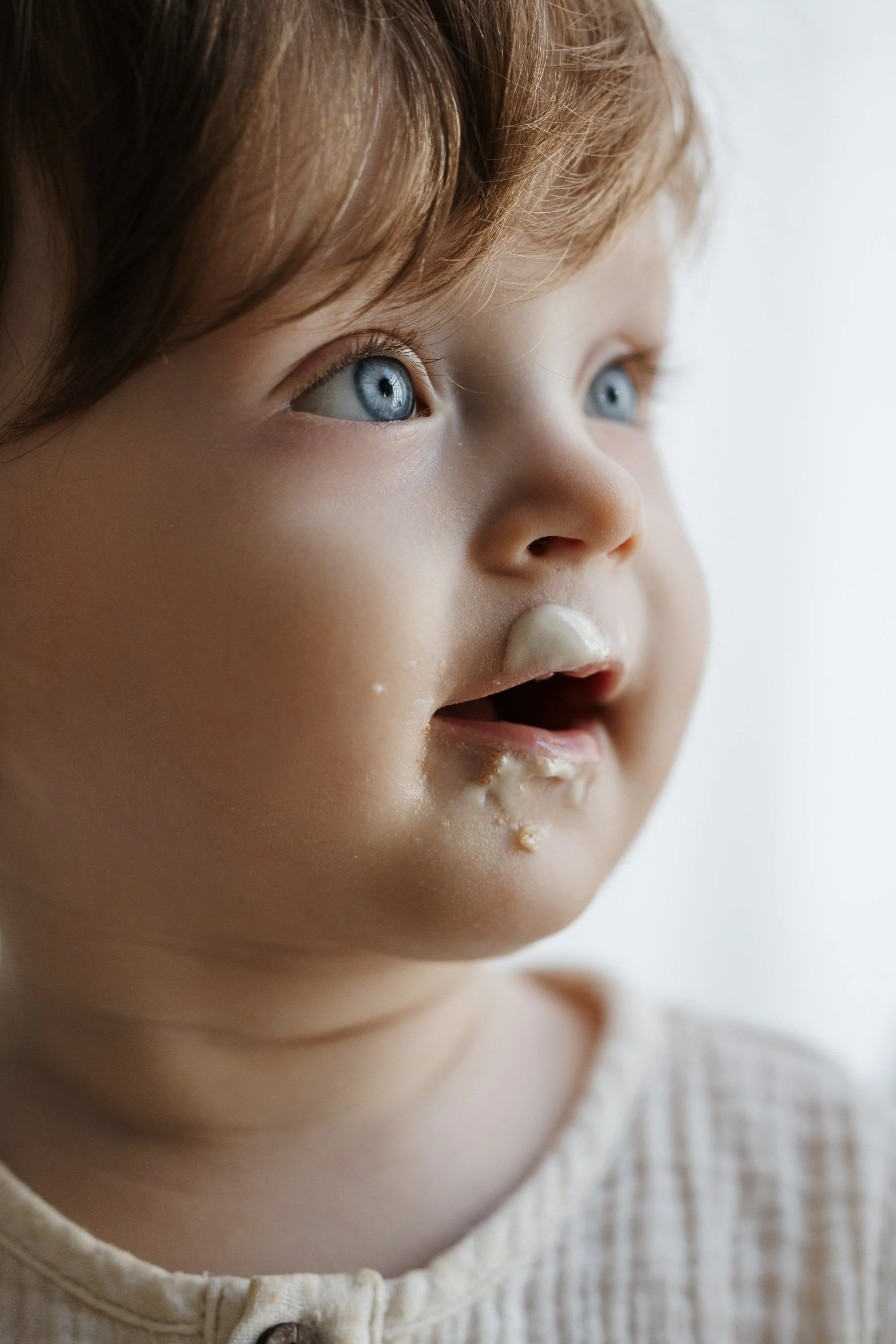 Close-up of a young child's face with blue eyes and light brown hair, showing remnants of food around the mouth.