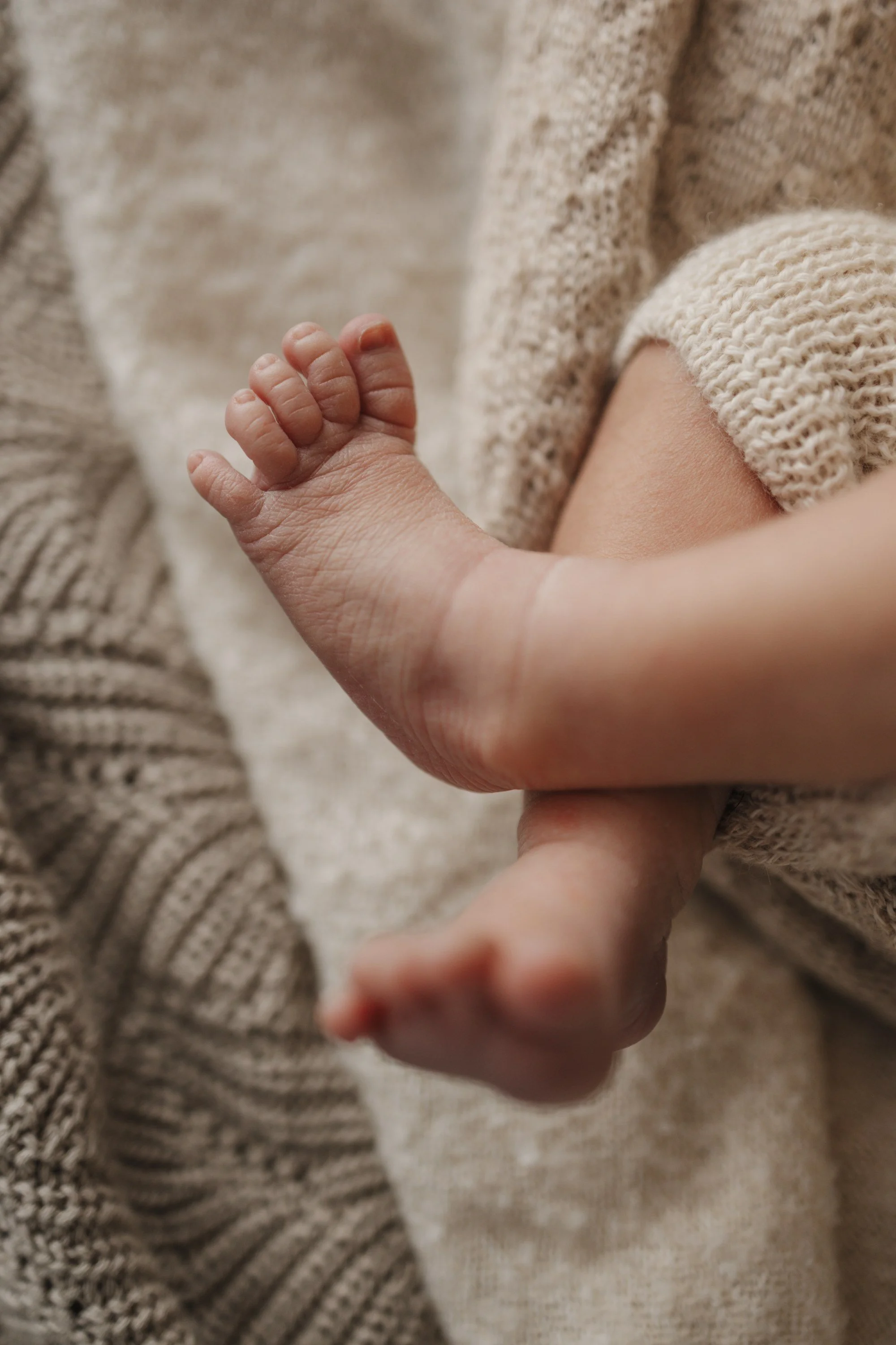 Close-up of a newborn baby's hand resting on a person's arm, both dressed in cozy, knitted clothing.