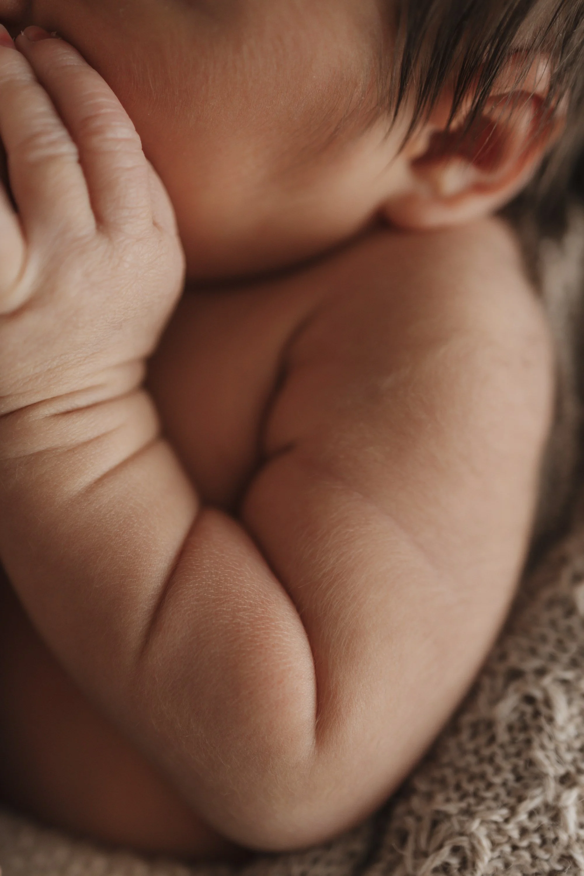 Close-up of a baby sleeping peacefully, curled up on a textured blanket.