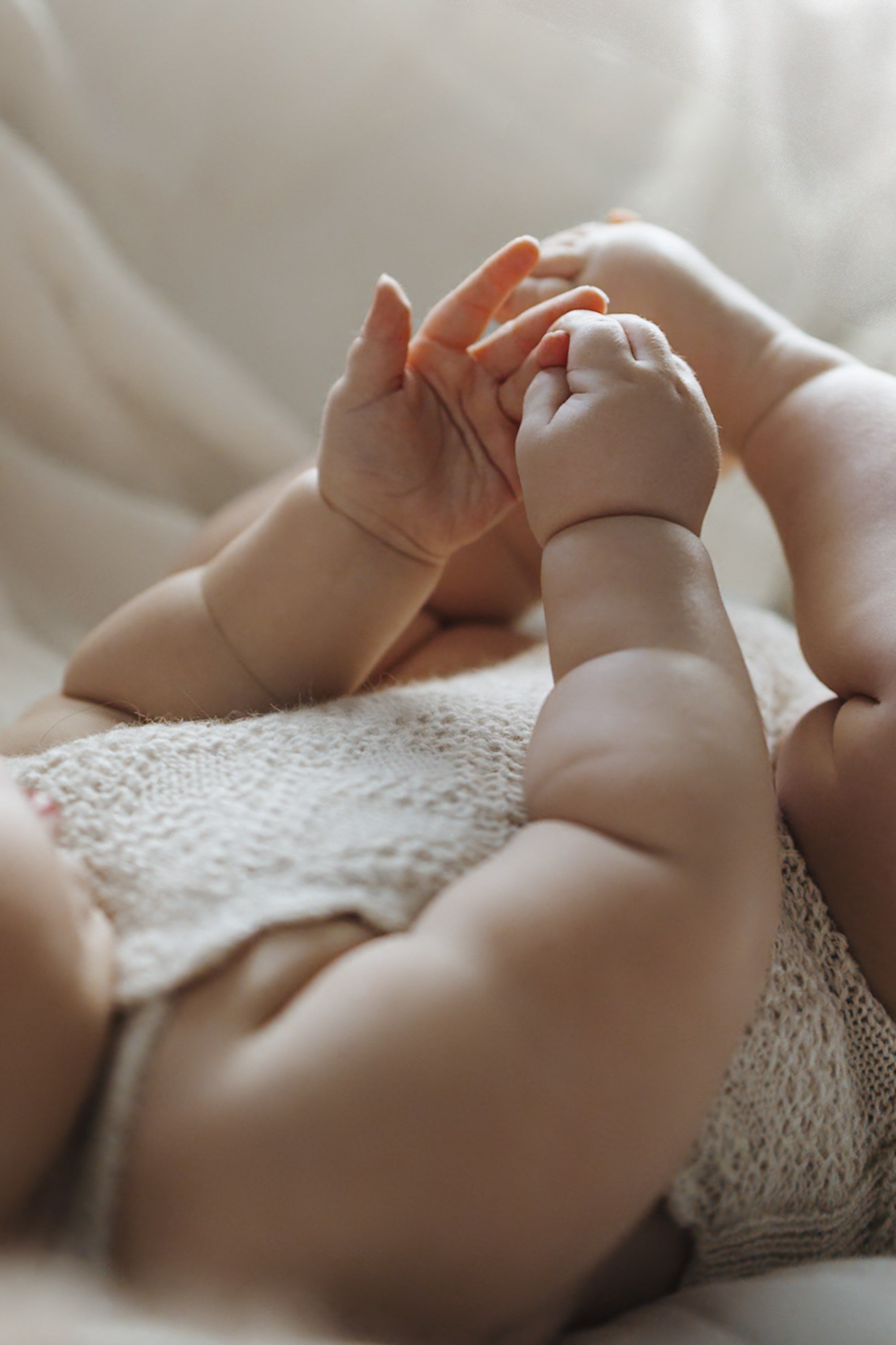 Close-up of a baby's hand grabbing an adult's finger, lying on a soft, textured blanket.