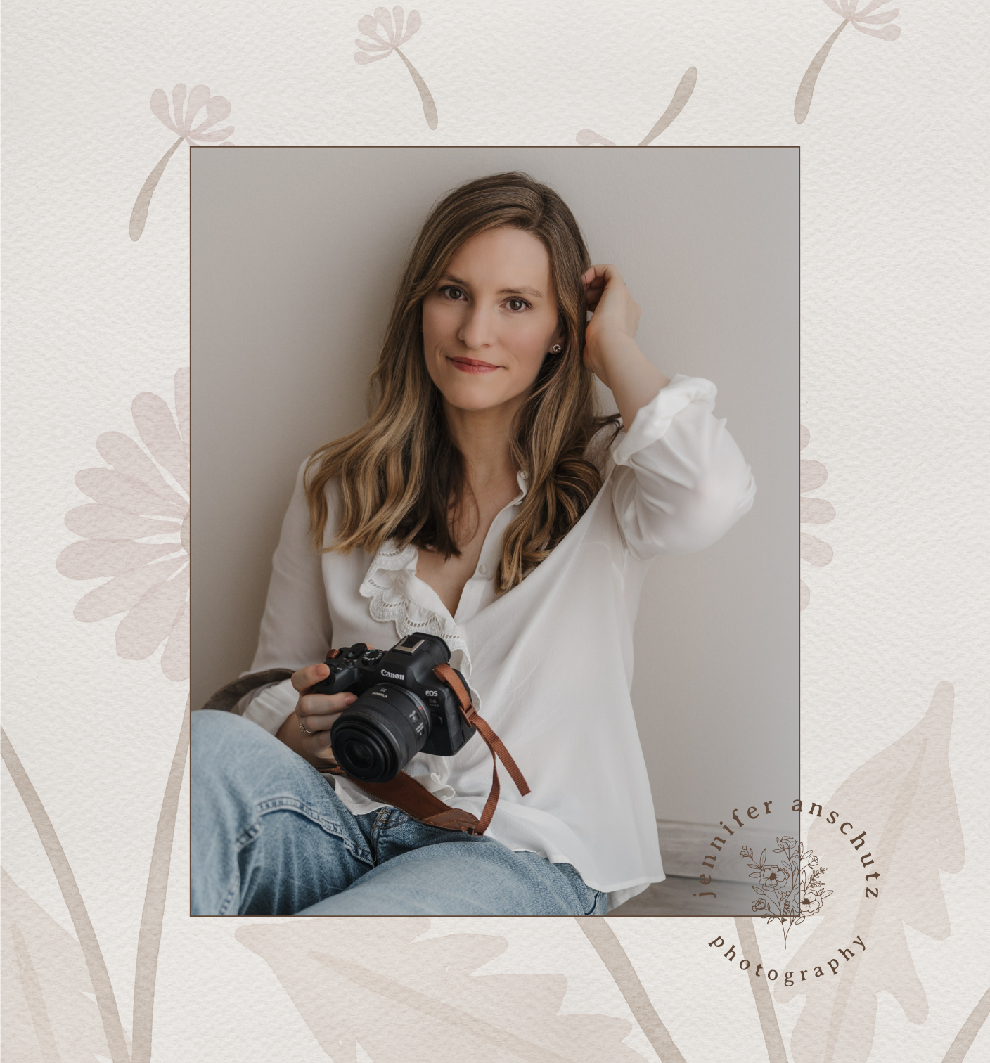 A woman with long brown wavy hair sitting against a plain light-colored wall, holding a Canon camera, and smiling at the camera. She is wearing a white blouse and blue jeans. The image has a decorative border with floral designs and her name, Jenniferanschütz, is written at the bottom right.