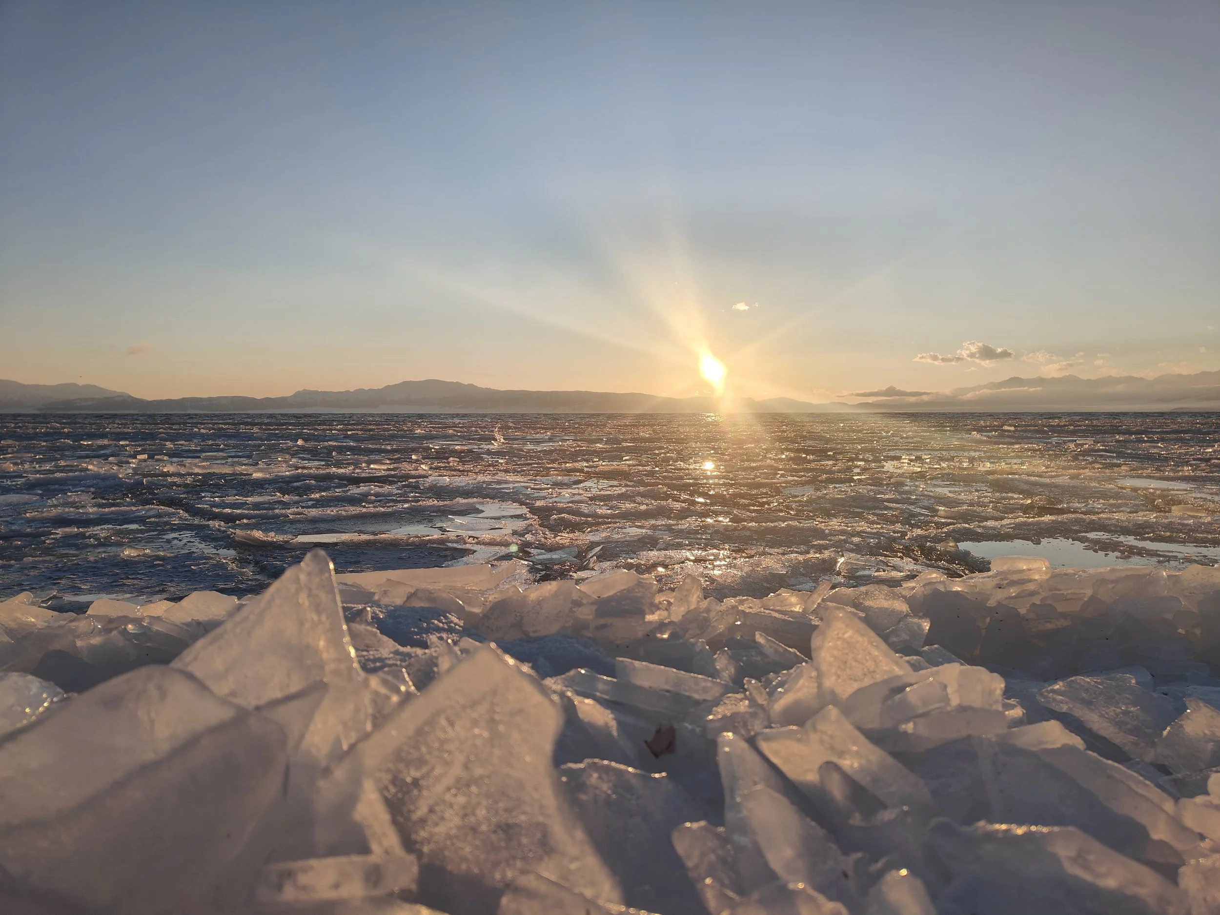 Sunset over a frozen icy landscape with mountains in the distance and clear sky. Hemu xinjiang