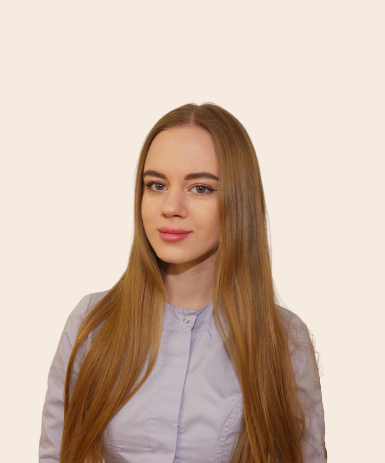 Young woman with long, straight red hair wearing a light gray shirt, standing against a plain, light-colored background.