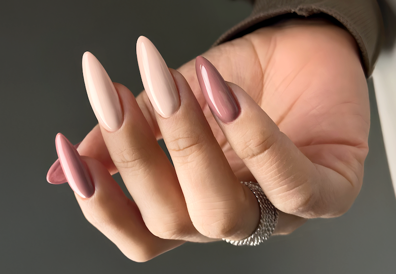 Close-up of a hand with manicured nails painted in shades of pink and nude, with a silver ring on the finger.