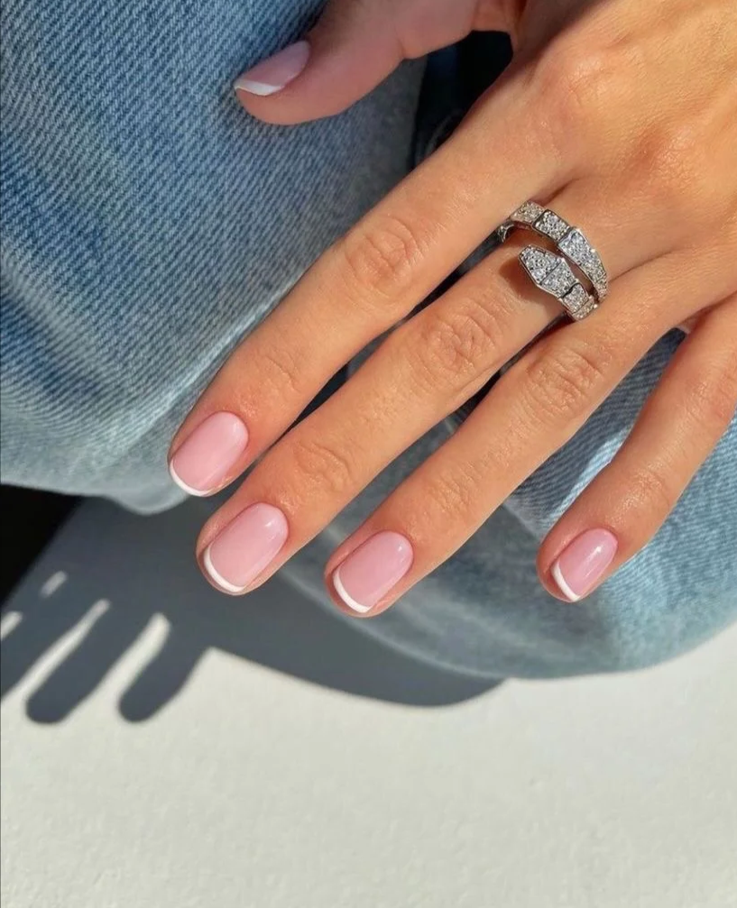 Close-up of a woman's hand with a diamond engagement ring and wedding band on her ring finger, resting on denim fabric.