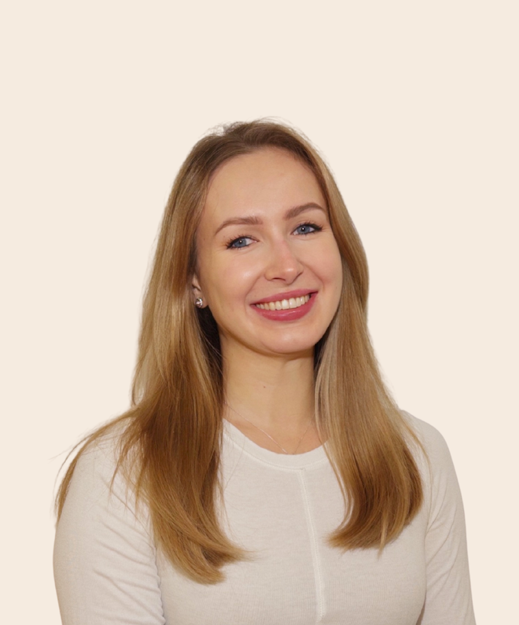 A woman with long, light brown hair smiles at the camera against a plain beige background.