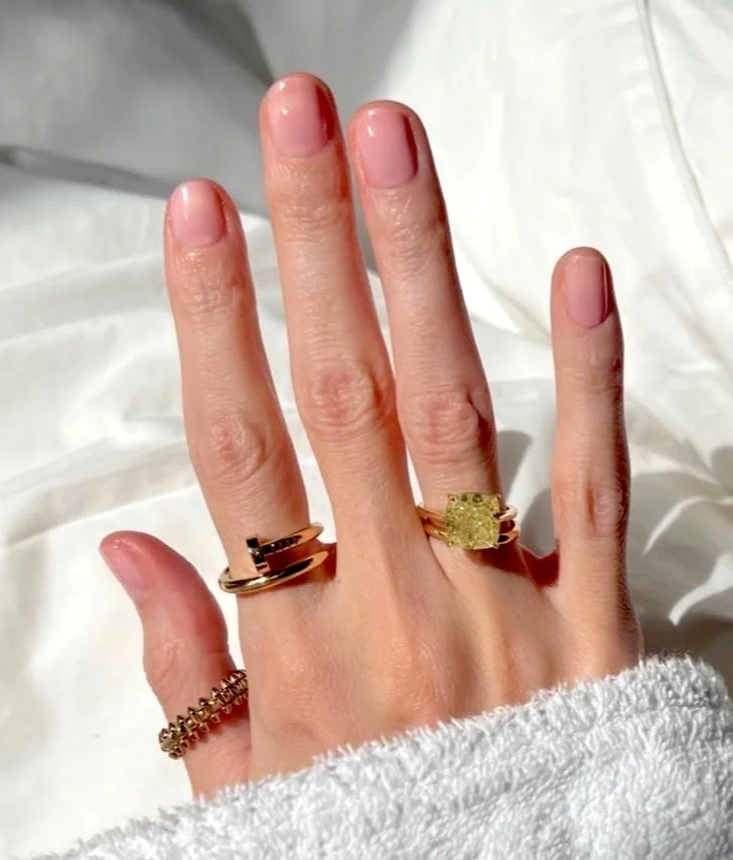 Close-up of a hand with three rings on fingers, one on the pinky, one on the middle finger, and one on the index finger, with a soft, white fabric background.