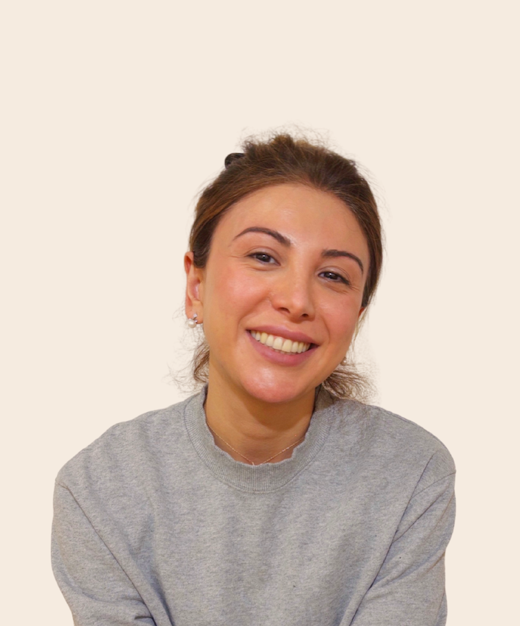 A smiling woman with brown hair in a ponytail, wearing a gray sweatshirt, against a plain light background.