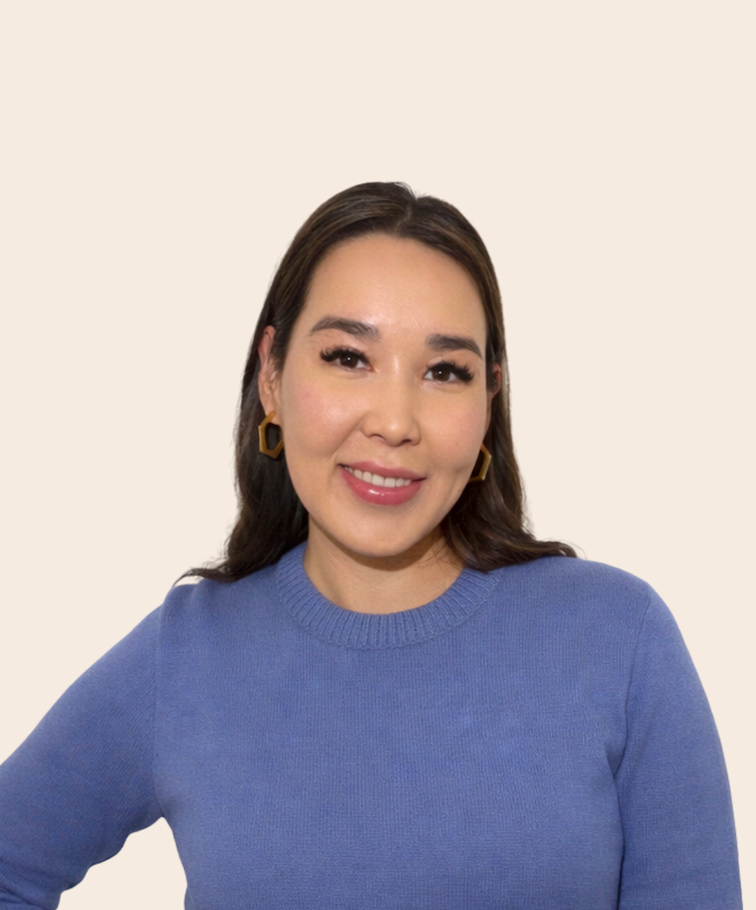 A woman with shoulder-length dark hair, wearing a blue sweater and gold geometric earrings, smiling at the camera against a plain light background.