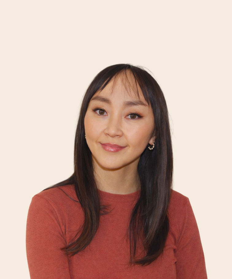 A woman with long dark hair, wearing a reddish-brown top and earrings, smiling at the camera against a plain light background.