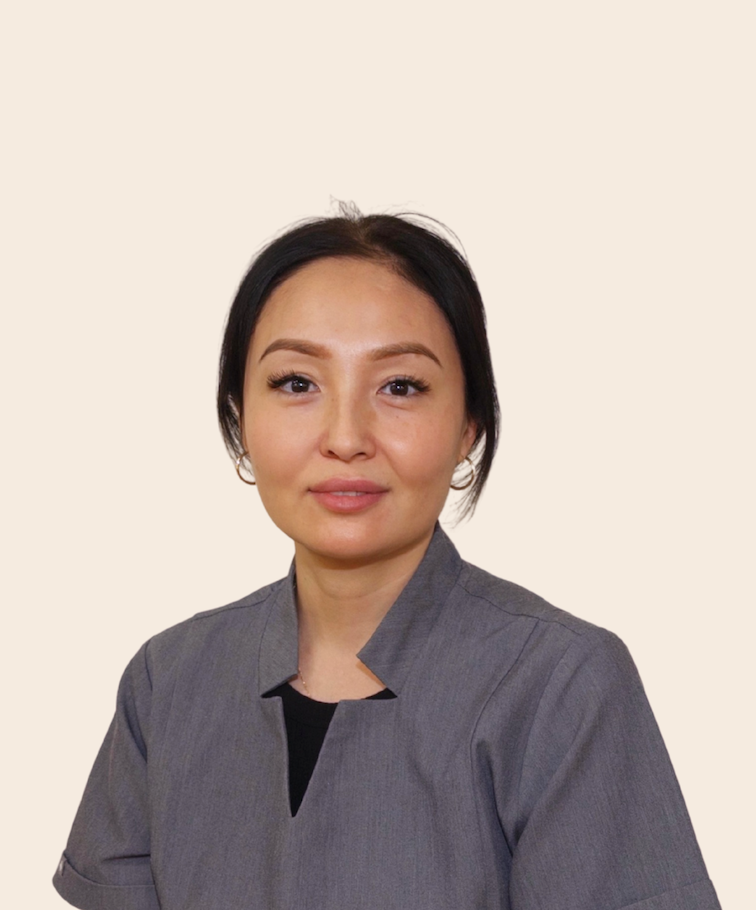 Portrait of a woman with dark hair, wearing a gray shirt, against a plain light-colored background.