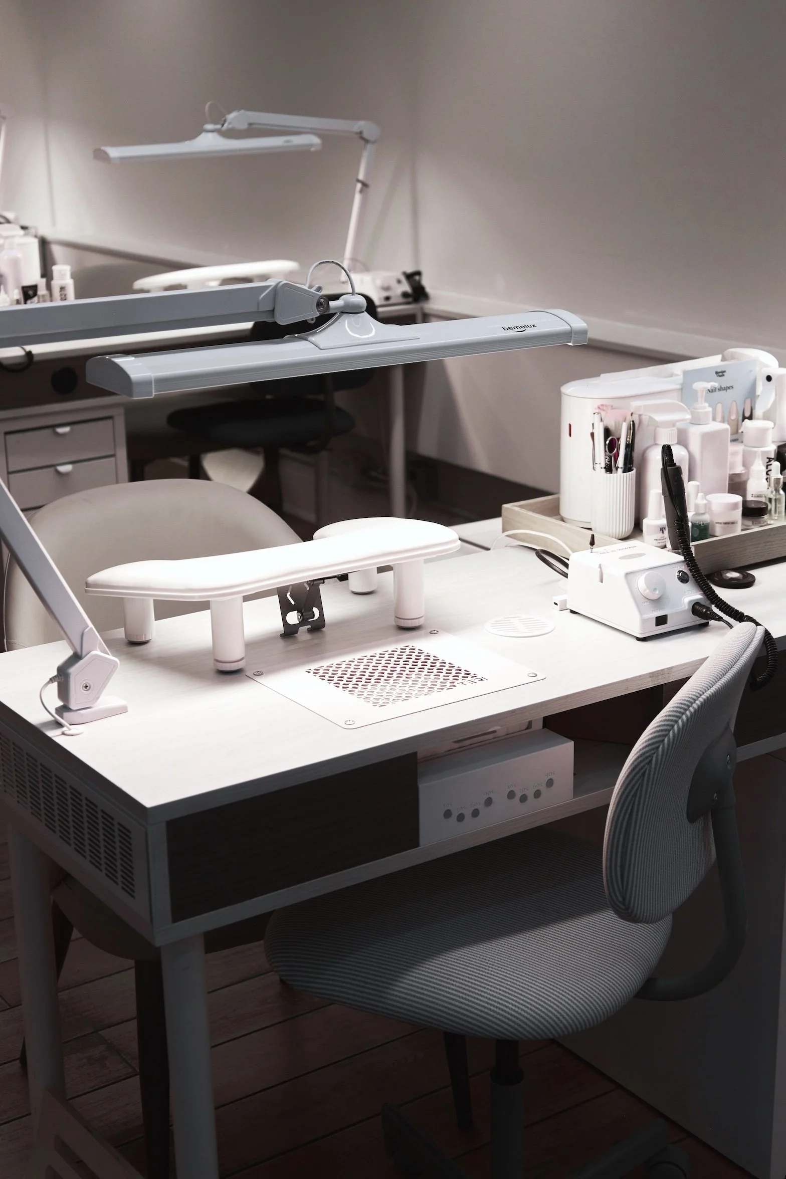 A manicure workspace with a white table, manicure tools, nail polish bottles, and desk lamps in a salon setting.