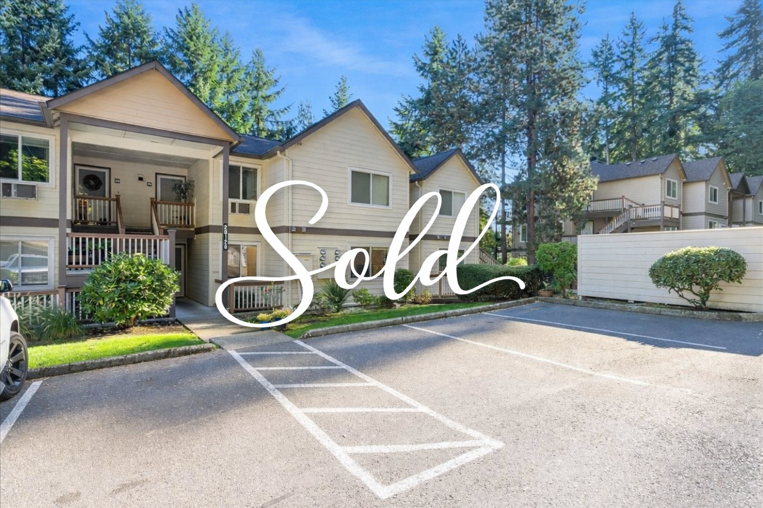 Multi-unit residential complex with parking lot and wood-paneled exterior, surrounded by tall pine trees, with a "Sold" overlay.