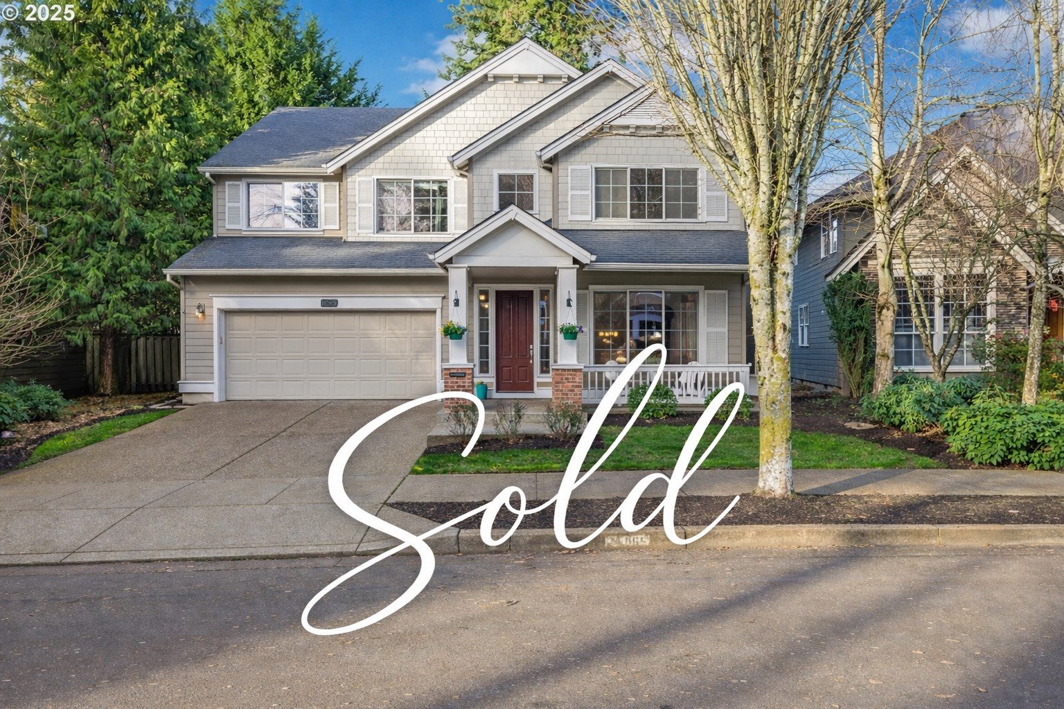Two-story house with gray siding, white trim, a front porch, and a garage. The yard has trees and shrubs. The word 'Sold' is overlaid on the image.