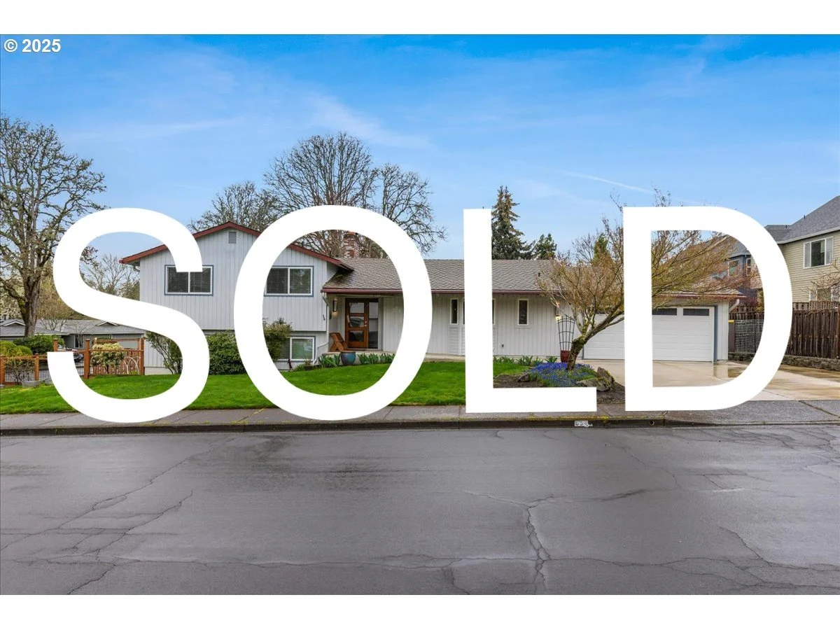 A suburban house with a white exterior and gray roof, front lawn, driveway, and trees. The word 'SOLD' is overlaid in large white letters.