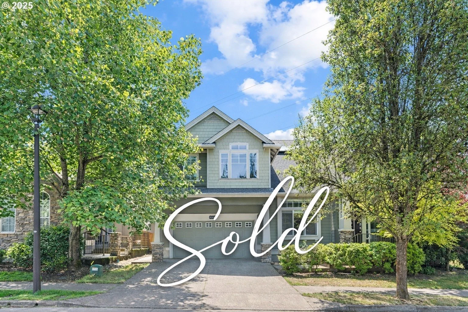 A two-story house with a garage, surrounded by trees, with a bright blue sky in the background and the word 'Sold' written in white text across the front.