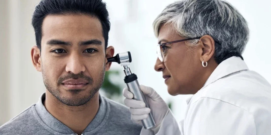 A healthcare professional examines a young man's ear with an otoscope.