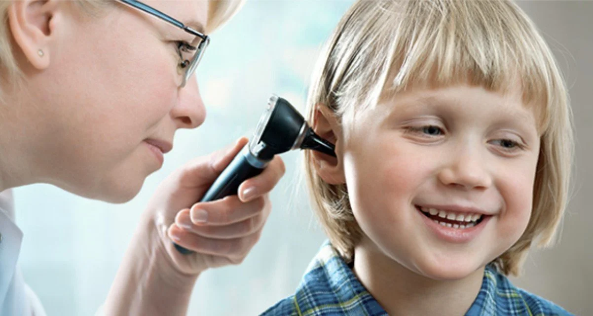 A healthcare professional examines a young boy's ear with an otoscope.