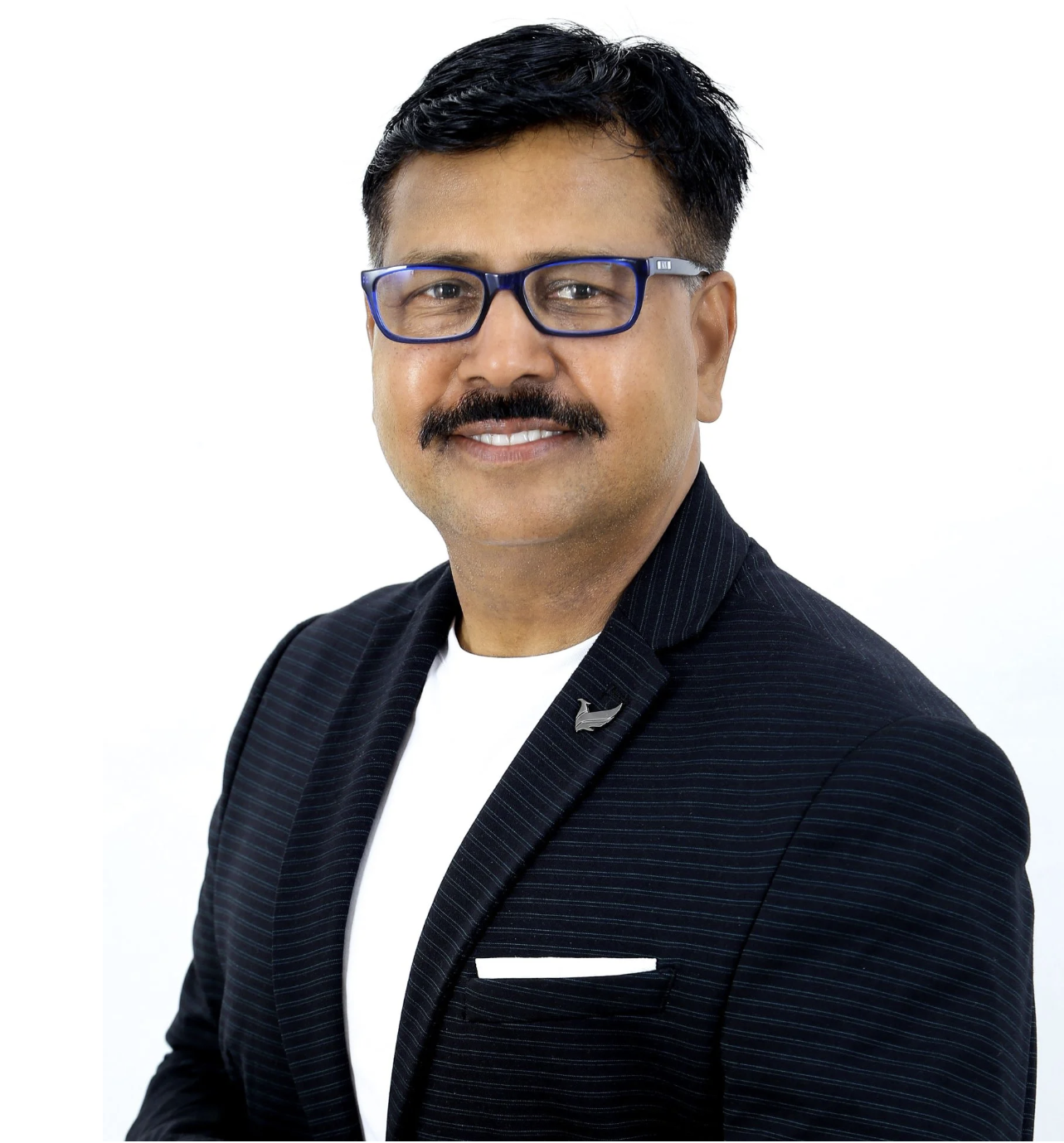Portrait of a man with black hair, glasses, a mustache, wearing a dark pinstripe blazer with a white shirt, smiling, against a plain white background.